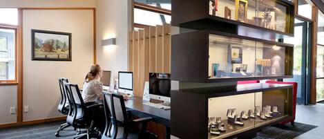 Un espacio de oficina moderno con una mesa larga, sillas y computadoras. Hay una vitrina con varios objetos.