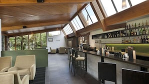 A spacious bar area with a high ceiling and skylights, a bar counter with stools, and a variety of bottles on shelves. - Scenic Hotel Franz Josef Glacier (Franz Josef Glacier)