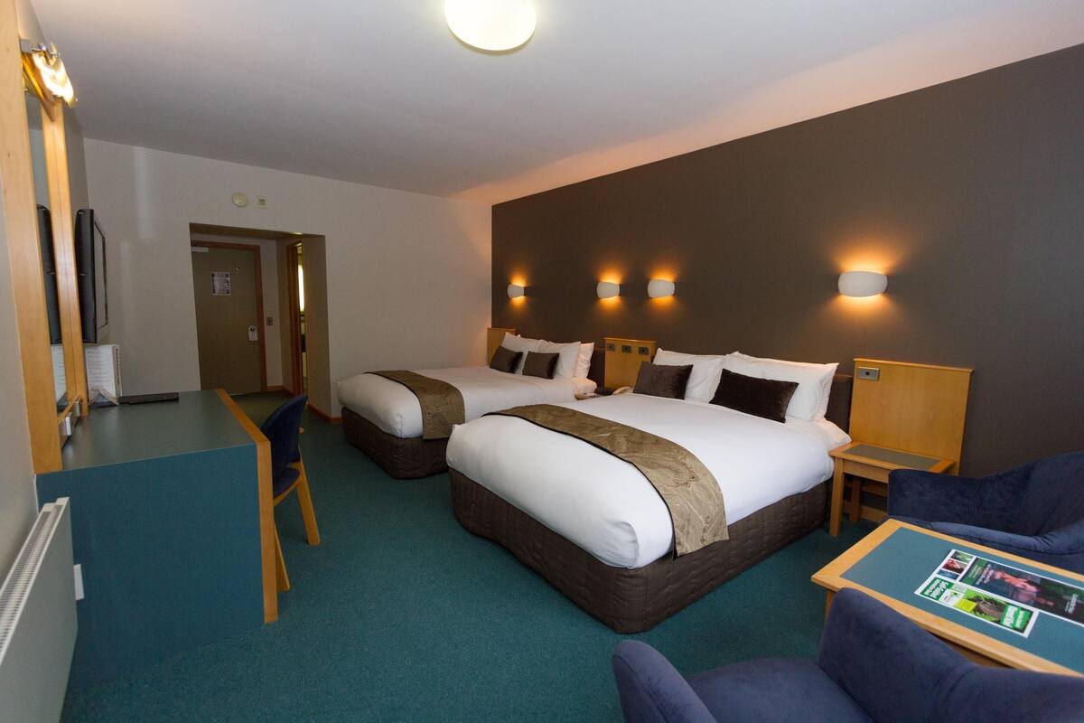 A hotel room with two beds, a desk, a chair, and a small table with a magazine.