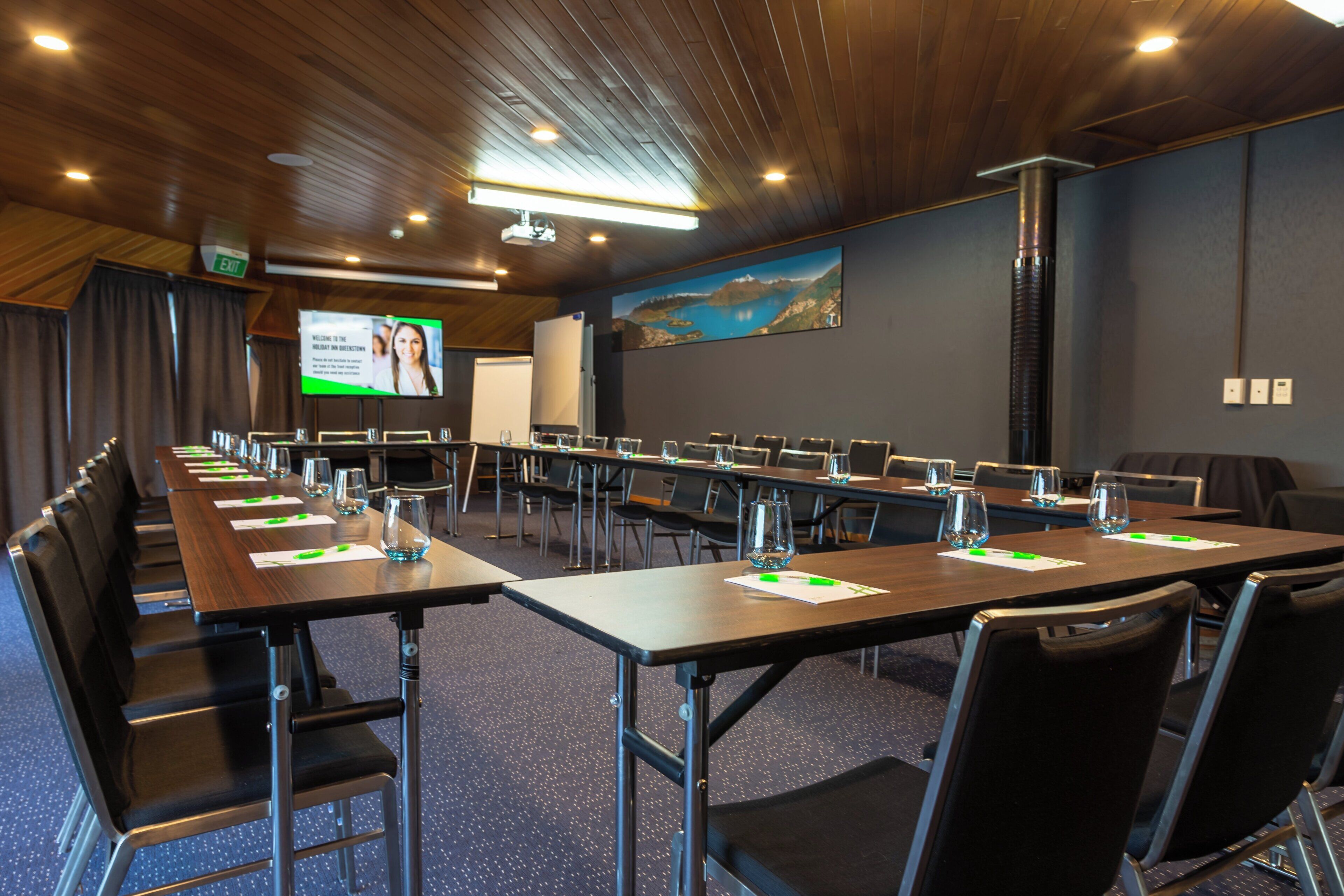 A conference room with long tables, chairs, and a projector screen.