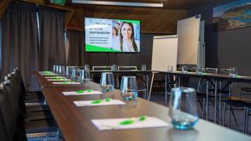Un salón de conferencias con una larga mesa, sillas, una pantalla que muestra un mensaje de bienvenida y una pizarra.