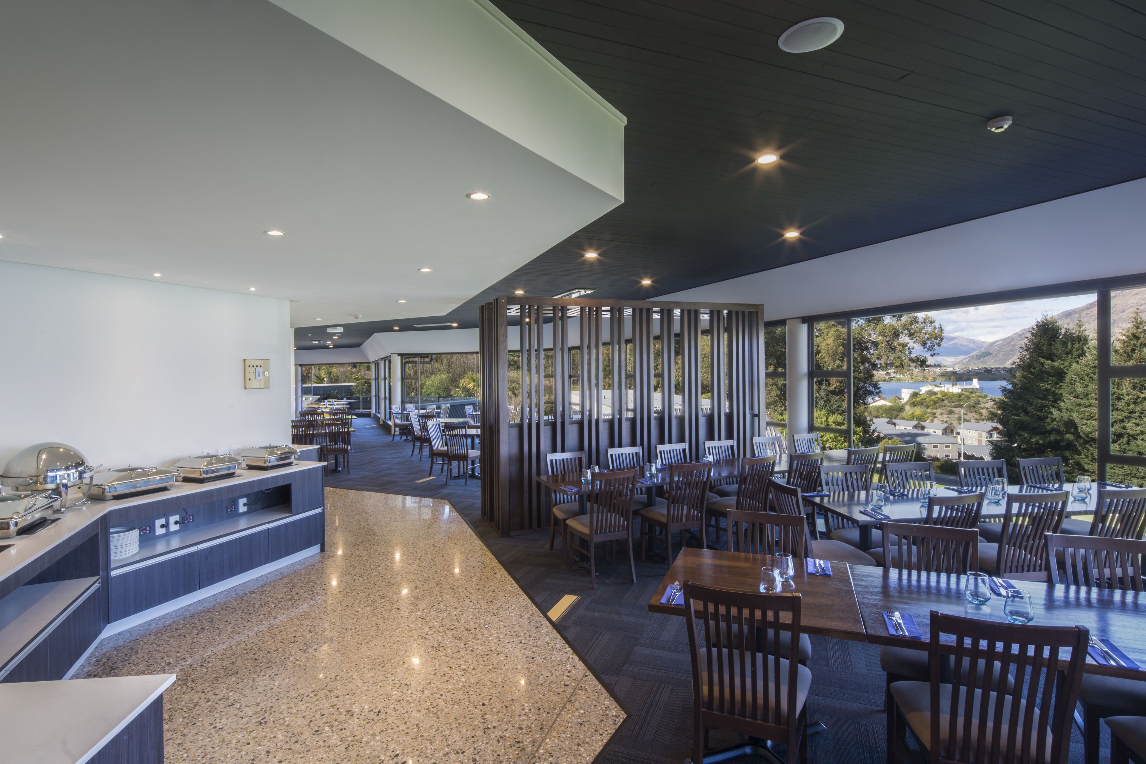 A modern restaurant with a long counter, multiple tables, and a view of the mountains.