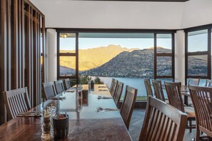 A dining area with a long table set for multiple guests, large windows offering a view of mountains and a lake, and wooden paneling on the walls. - Holiday Inn Queenstown Frankton Road by IHG (Queenstown)