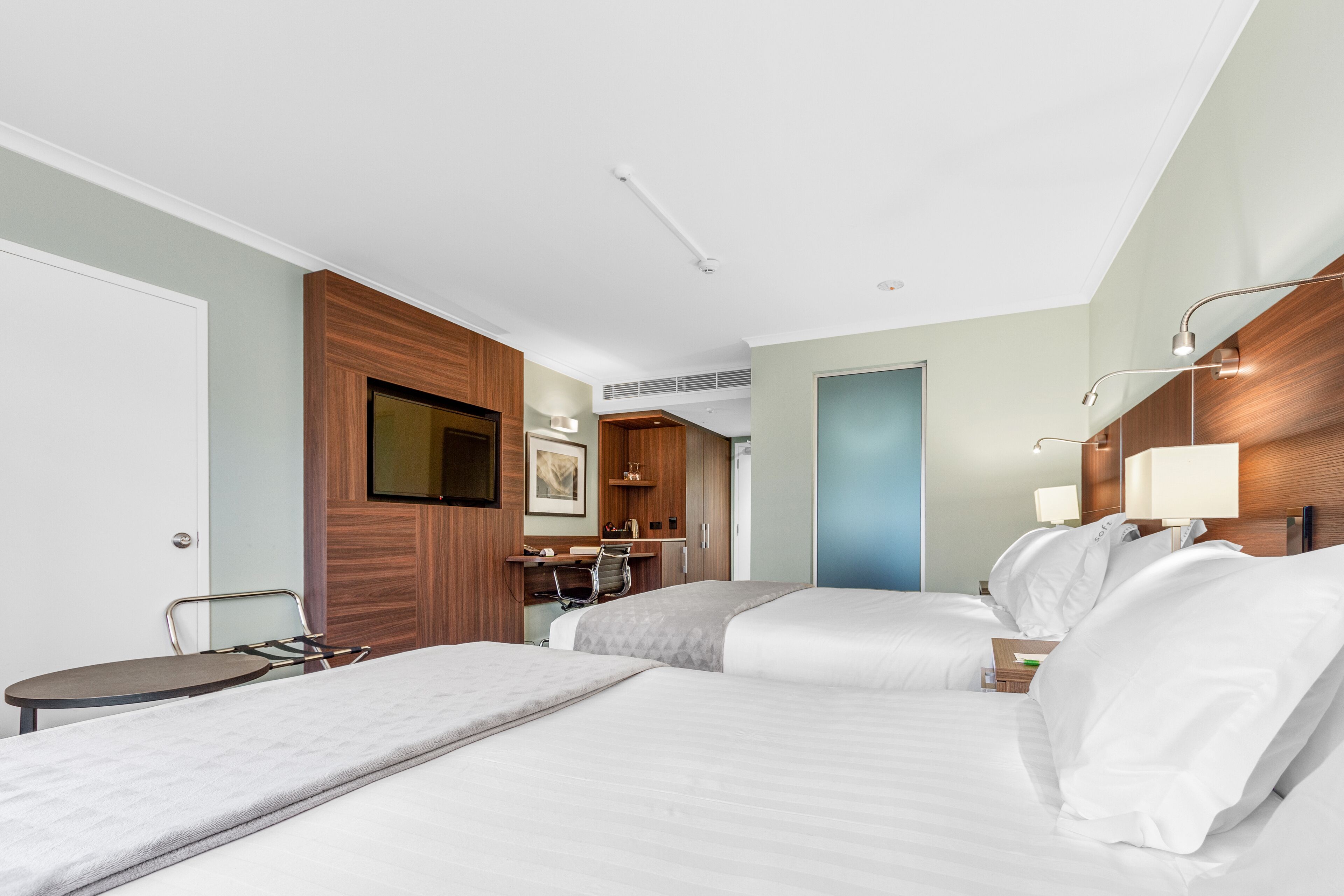 A hotel room with two beds, a desk, a chair, a TV, and a bathroom visible through an open door.