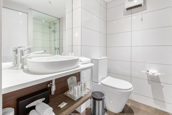 Un baño moderno con un lavamanos grande blanco, un espejo, un inodoro y un cubo de basura.