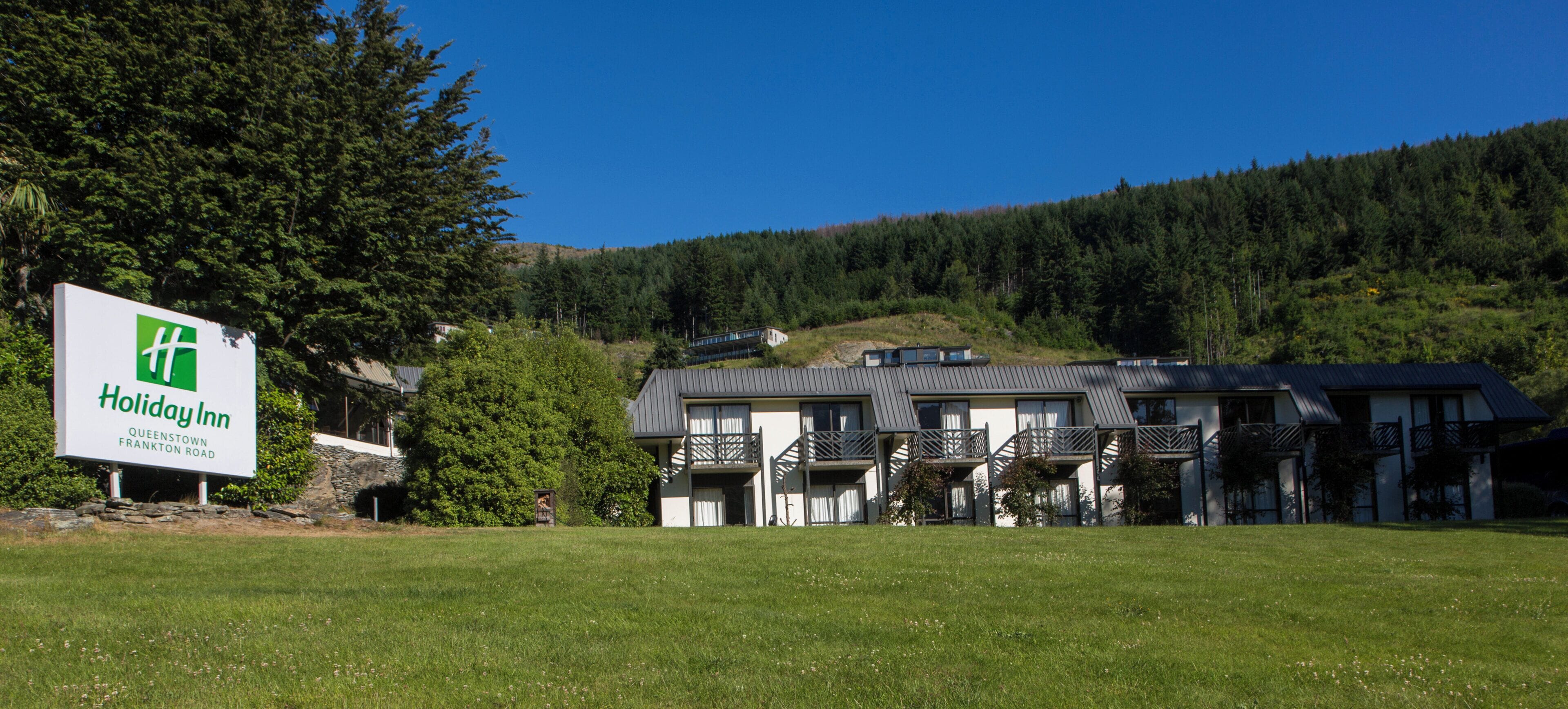 A Holiday Inn Queenstown Frankton Road with a grassy lawn and a mountain backdrop.