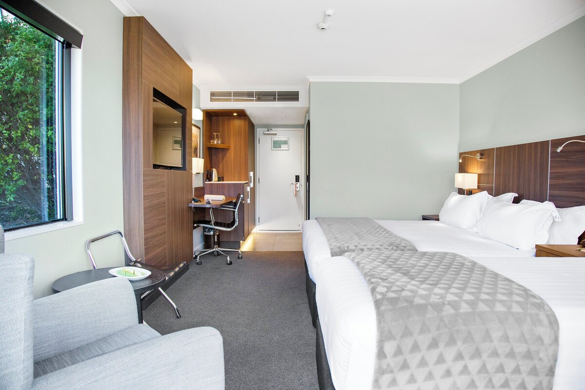 A hotel room with a bed, a desk, a chair, and a window.