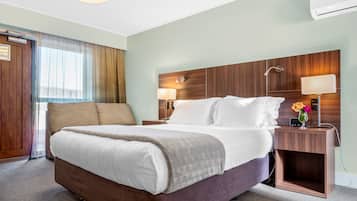 Ein Hotelzimmer mit einem großen Bett, einem hölzernen Kopfteil, zwei Nachttischen mit Lampen und einem Fenster mit Vorhängen.