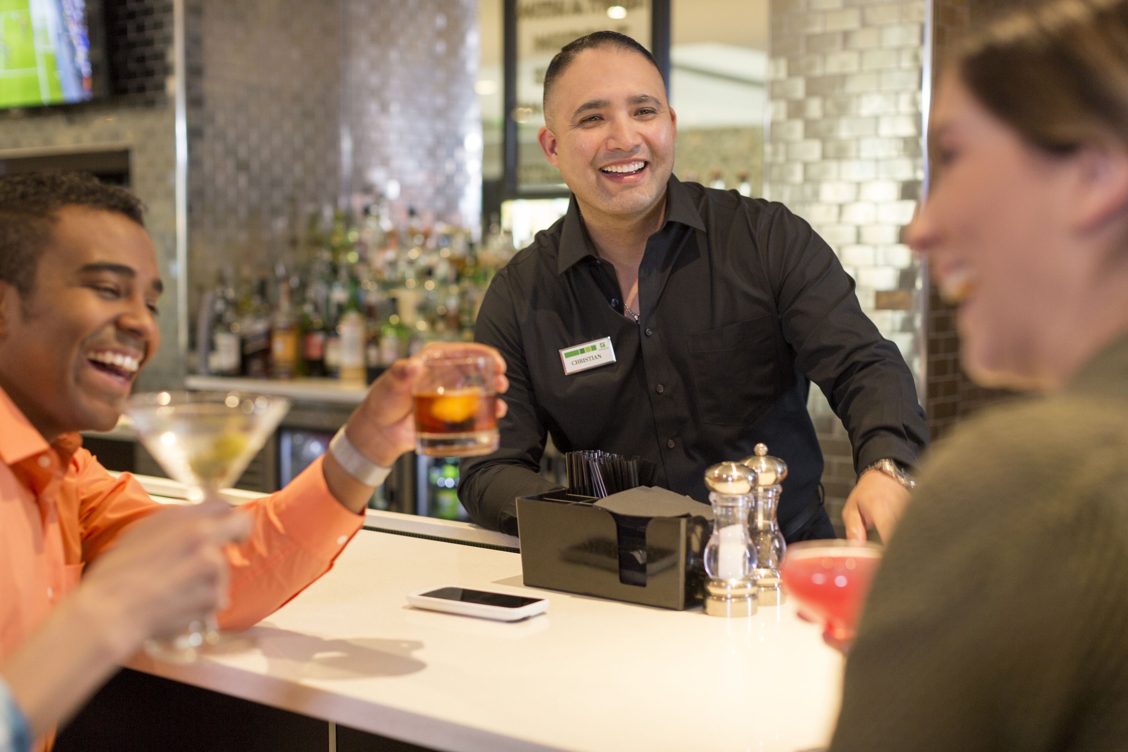 A bar area with a counter, a name tag, a smartphone, and a drink.