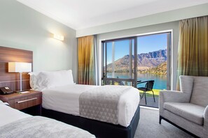 A hotel room with a bed, a desk with a phone, a chair, and a view of a lake and mountains. - Holiday Inn Queenstown Frankton Road by IHG (Queenstown)