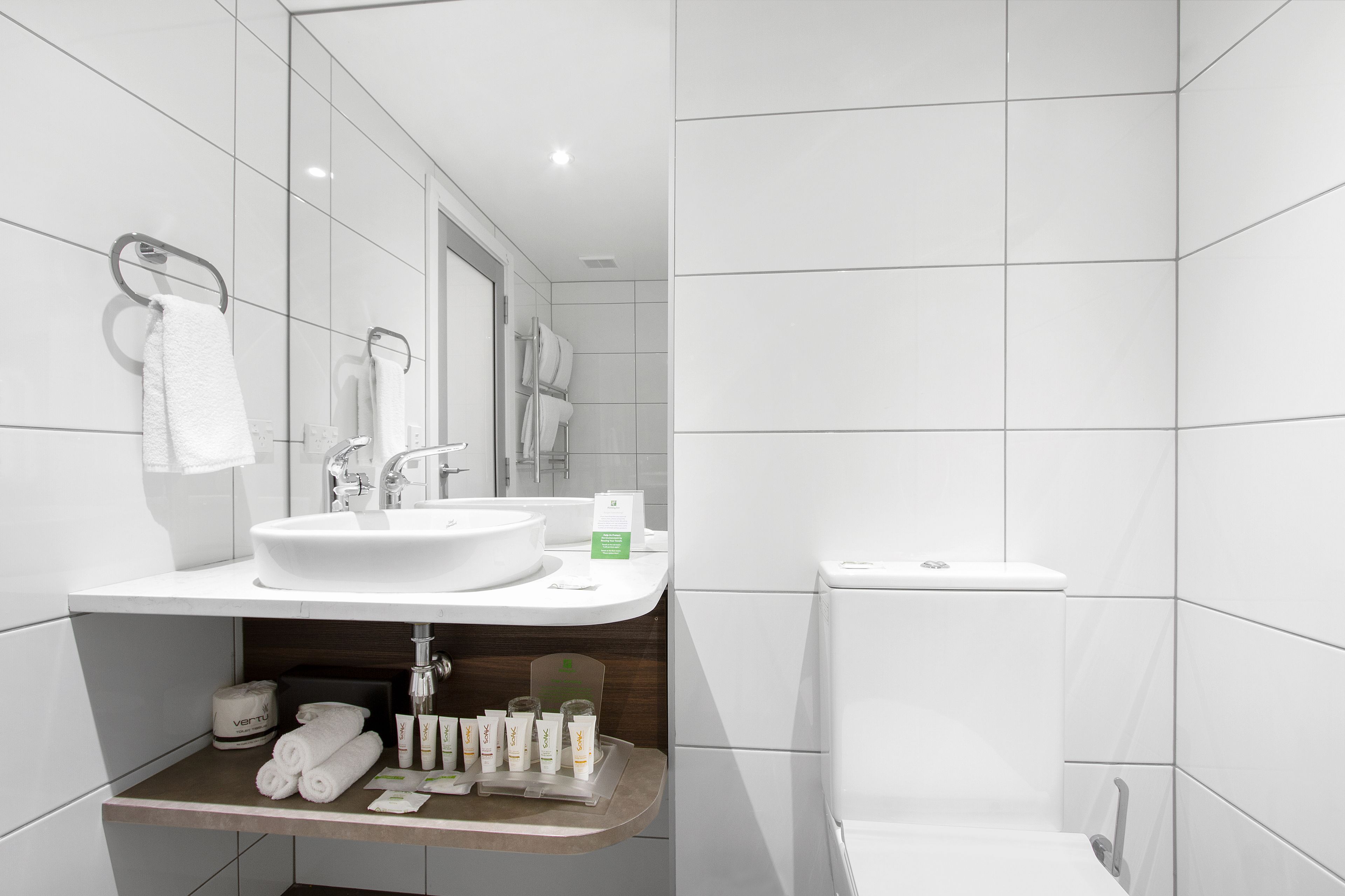 Een moderne badkamer met een wit wastafelmeubel, spiegel en toilet. Handdoeken en toiletartikelen liggen op het aanrecht.