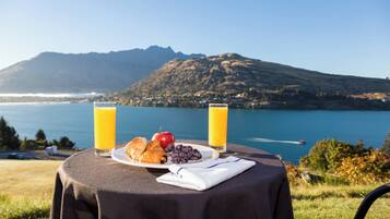 Una mesa con alimentos para el desayuno y dos vasos de jugo de naranja, con vistas a un lago y montañas.