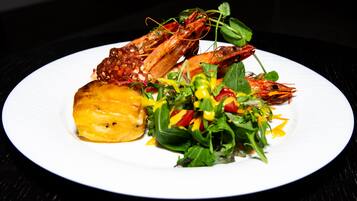 A plate with grilled shrimp, a slice of pineapple, and a mixed greens salad.