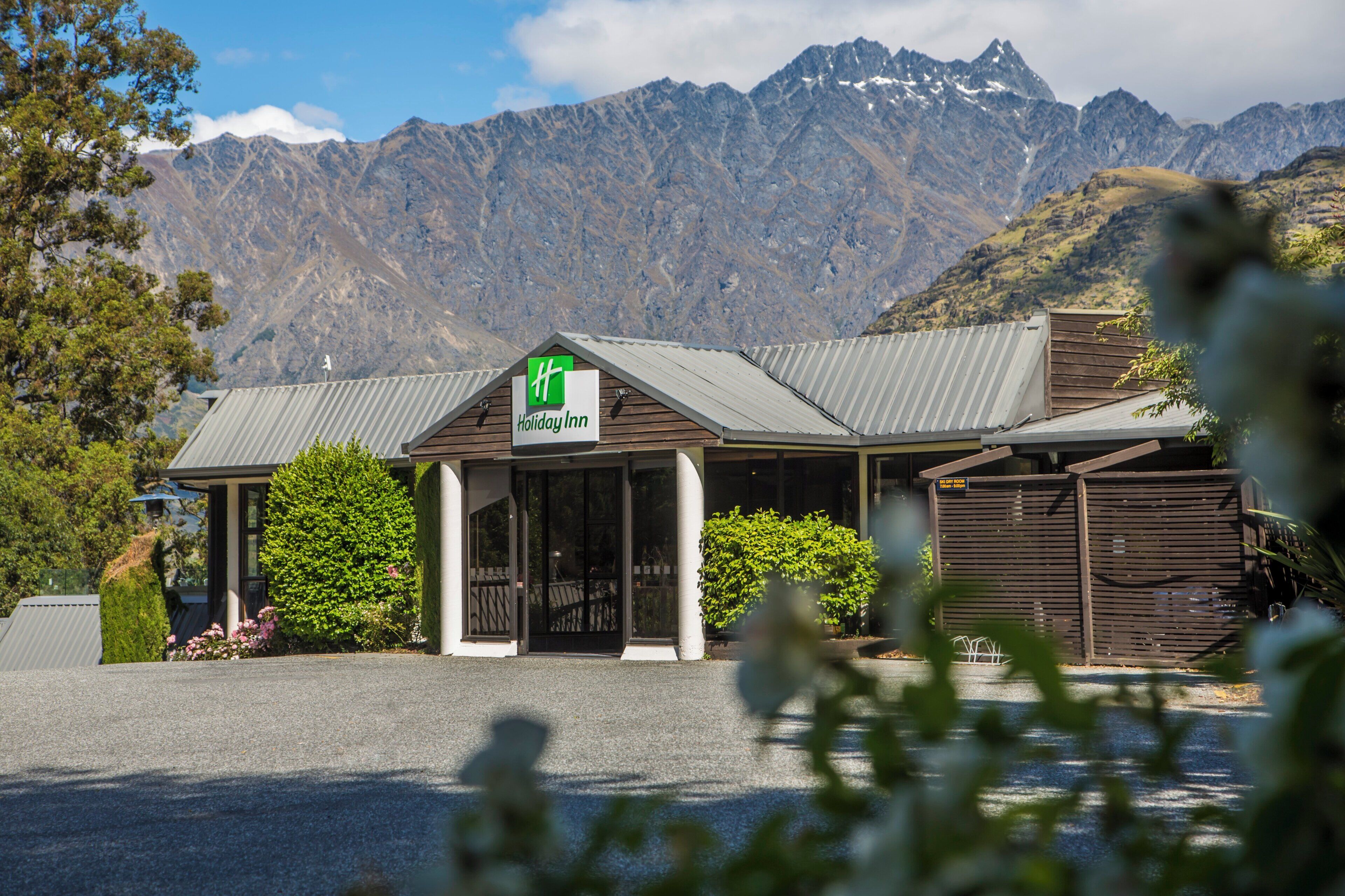 A Holiday Inn with a mountain backdrop, featuring a well-maintained garden and a clear sky.