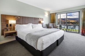 A hotel room with a large bed, a desk with a lamp, a chair, and a view of a lake through a large window. - Holiday Inn Queenstown Frankton Road by IHG (Queenstown)