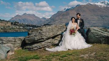 A couple in wedding attire by a lake with mountains in the background.