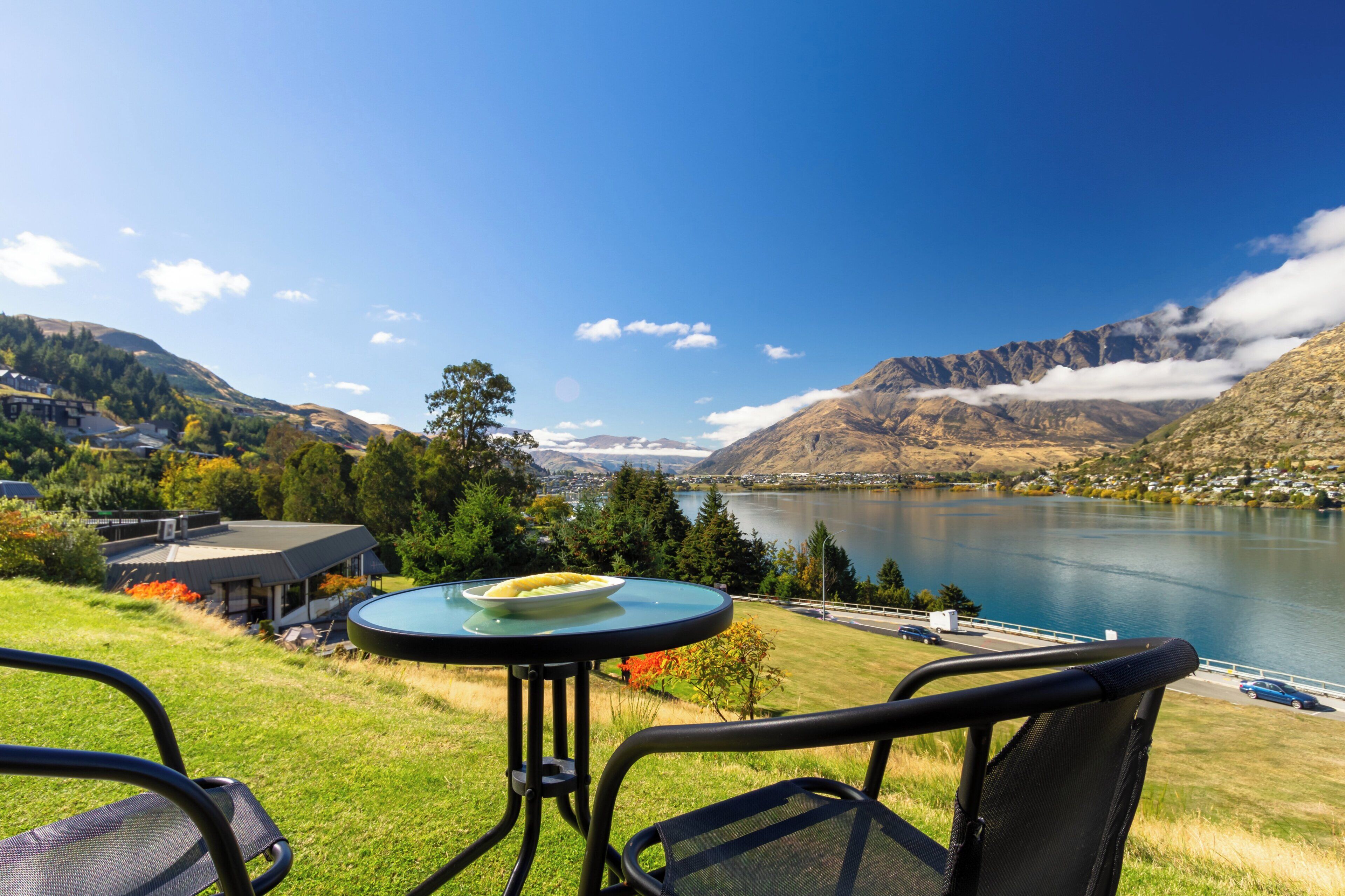 A table with a plate of food, overlooking a lake with mountains in the background.