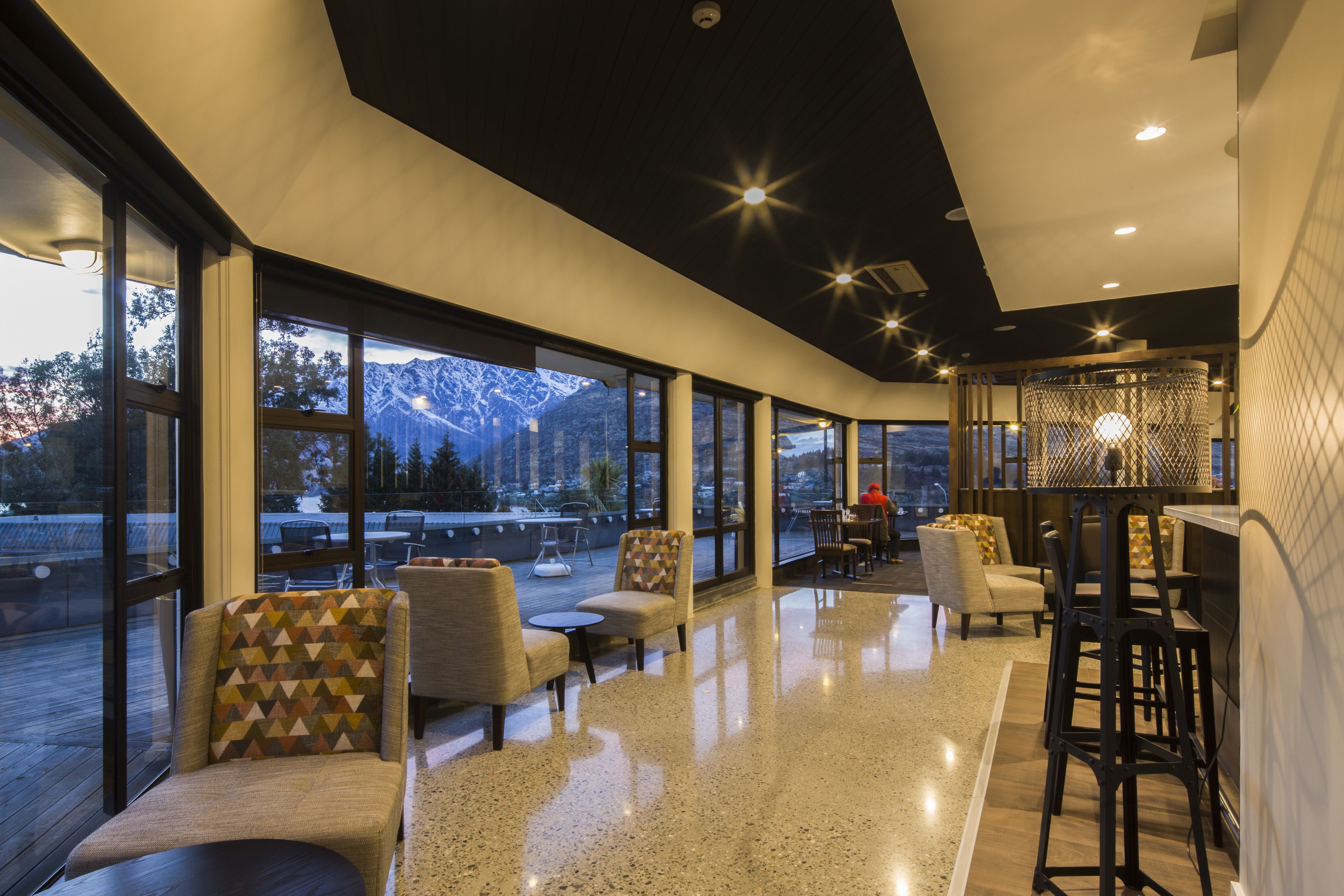 Un espacio lounge moderno con amplios ventanales, asientos y una zona de bar.
