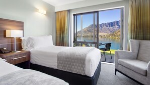 A hotel room with a bed, a desk with a lamp, a chair, and a view of a lake and mountains. - Holiday Inn Queenstown Frankton Road by IHG (Queenstown)