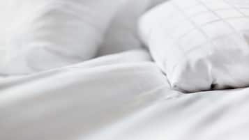 A close-up of a bed with white bedding and a pillow with a grid pattern.