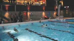 Una piscina con carriles, un puesto de socorrista y una zona de estar con sillas.