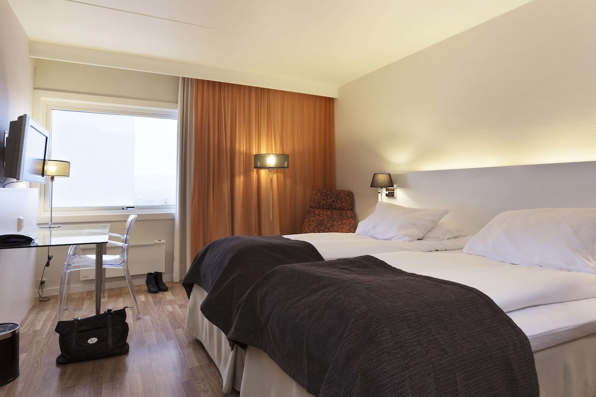 A hotel room with two beds, a desk, a chair, and a TV.