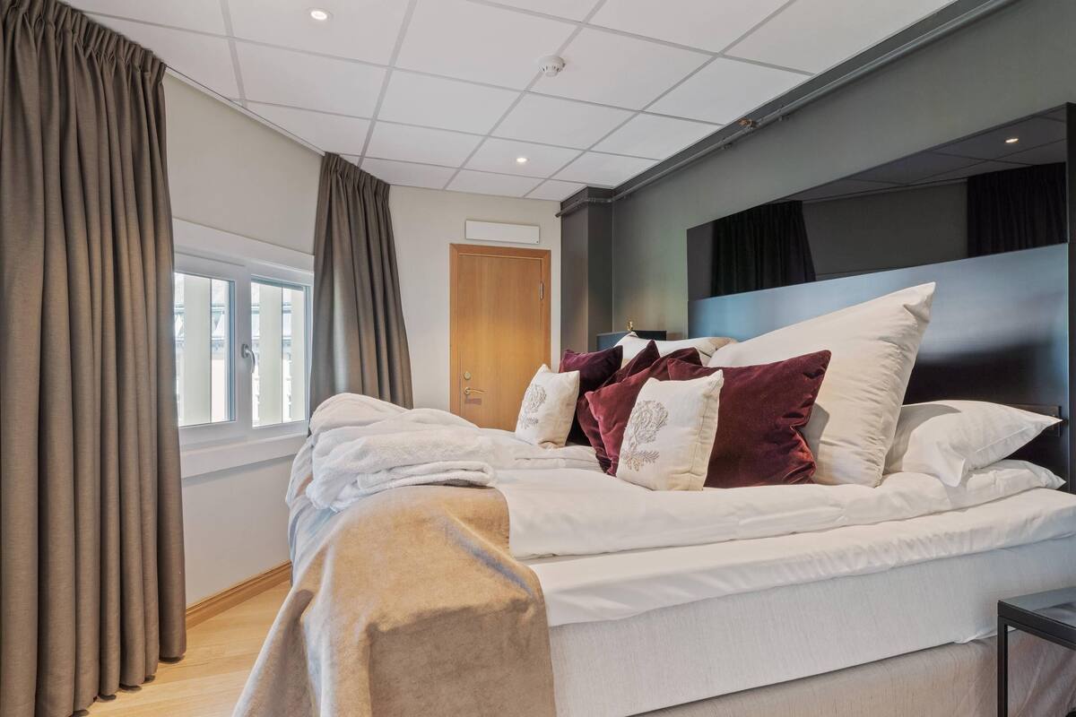 A modern hotel room with a large bed, a headboard, and a window with curtains.