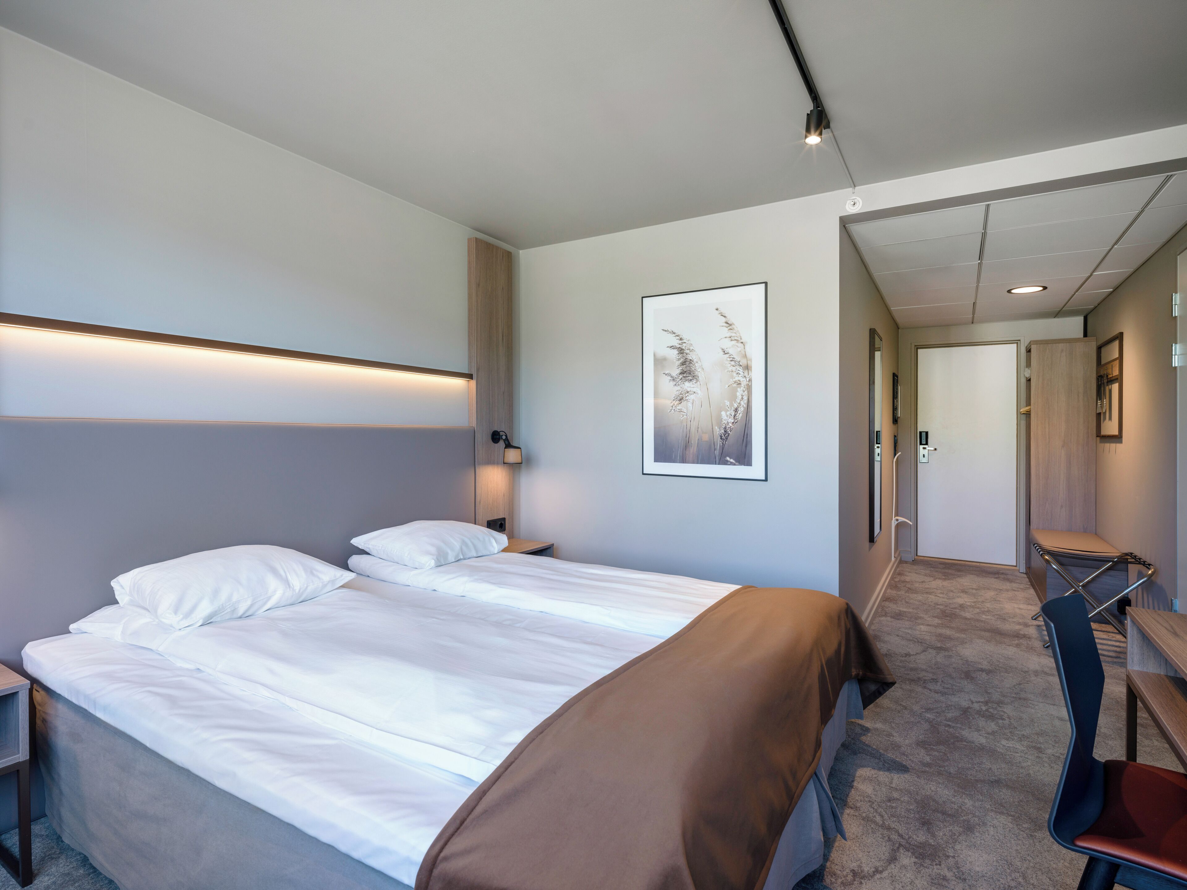 Ein Hotelzimmer mit einem großen Bett, einem Schreibtisch und einem Stuhl. Eine Tür führt in einen weiteren Raum.
