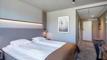 Ein Hotelzimmer mit einem großen Bett, einem Schreibtisch und einem Stuhl. Eine Tür führt in einen weiteren Raum.