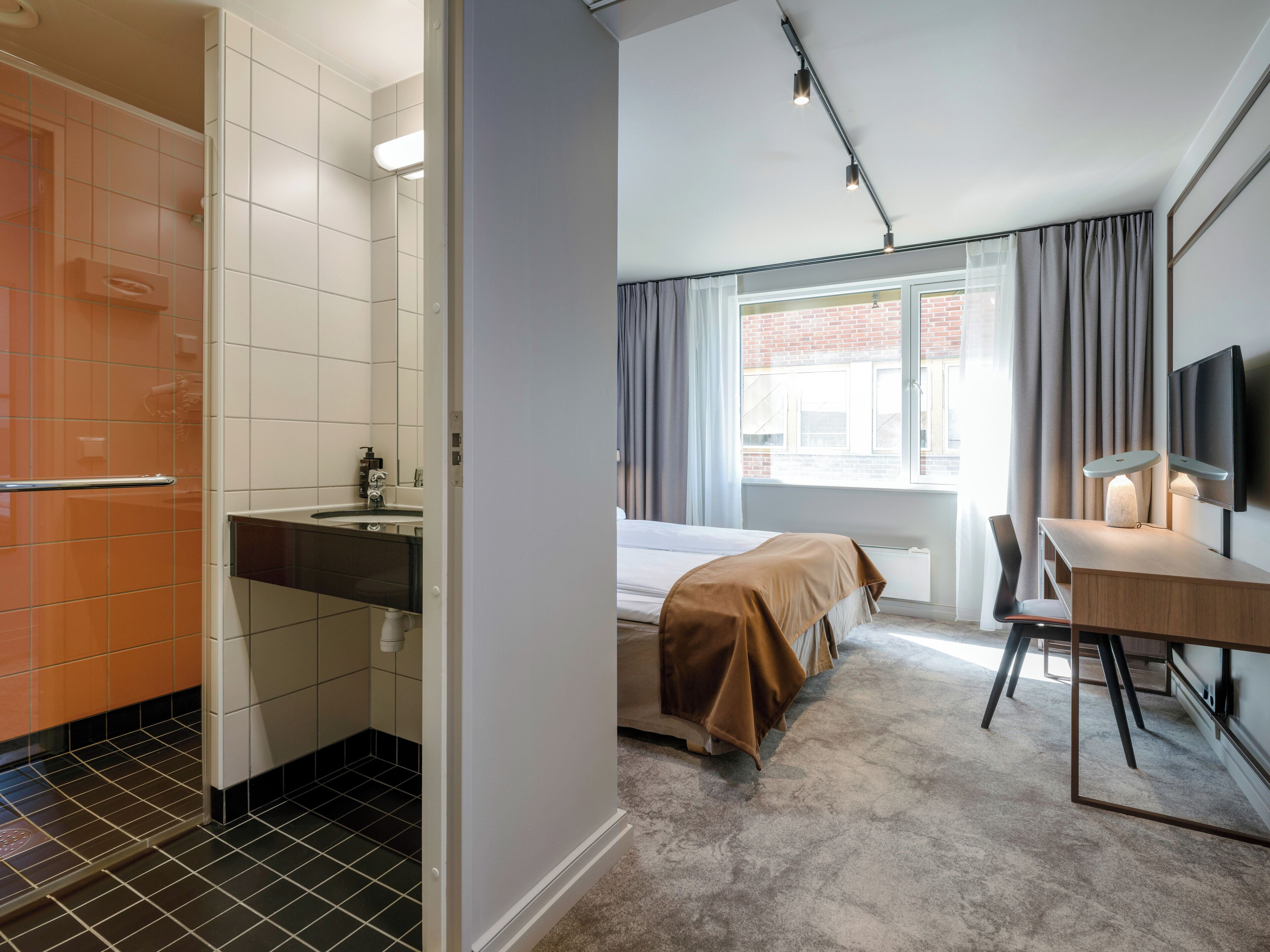 Una habitación de hotel con baño, cama, escritorio y televisor.