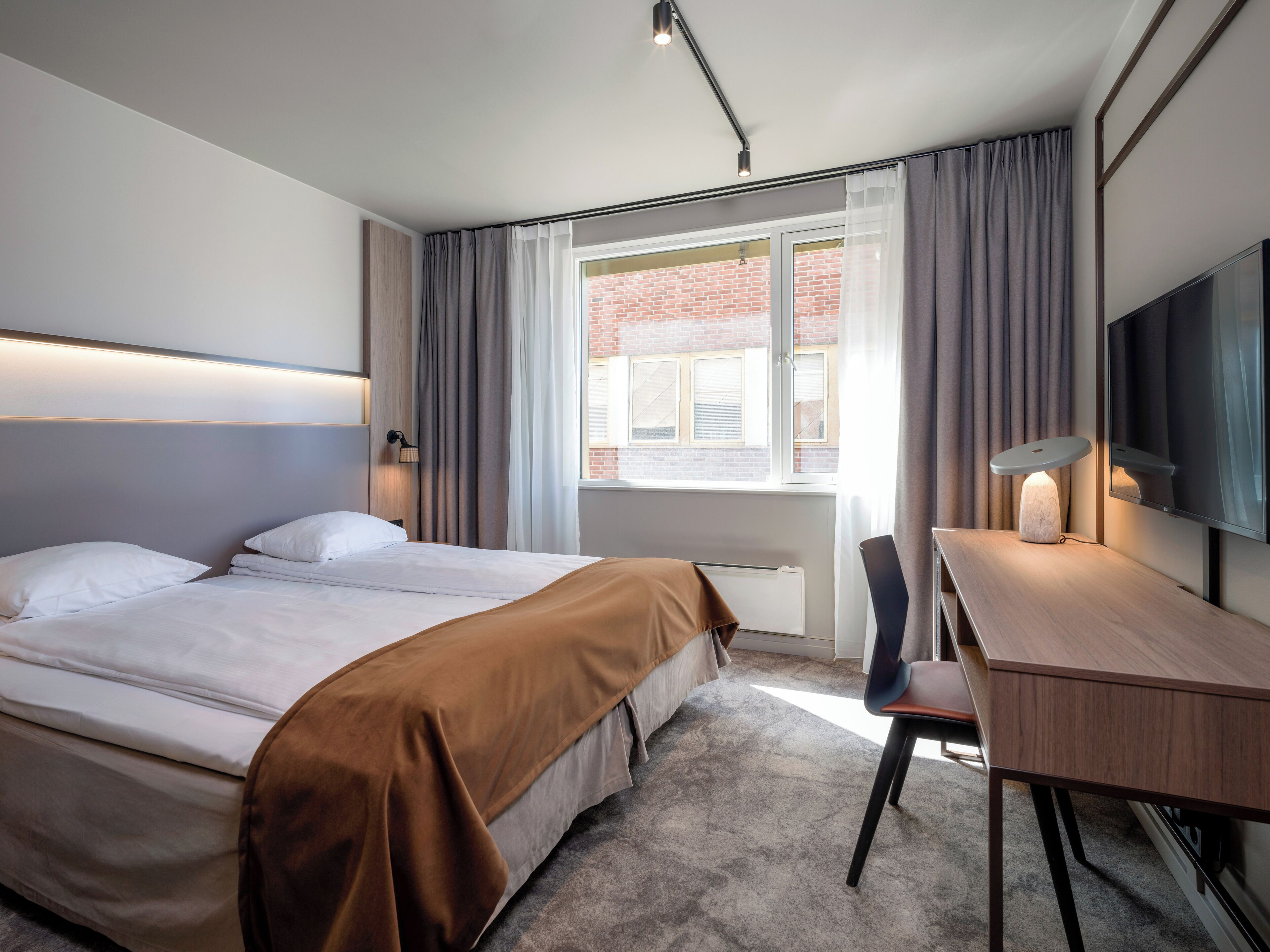 Una habitación de hotel moderna con una cama grande, un escritorio con lámpara y un televisor montado en la pared.