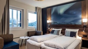 A hotel room with a bed, two chairs, a small table, and a large window. - Quality Hotel Saga (Tromsø)
