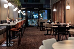 A restaurant with long communal tables and booths, a carpeted floor, and hanging pendant lights. - Quality Hotel Saga (Tromsø)