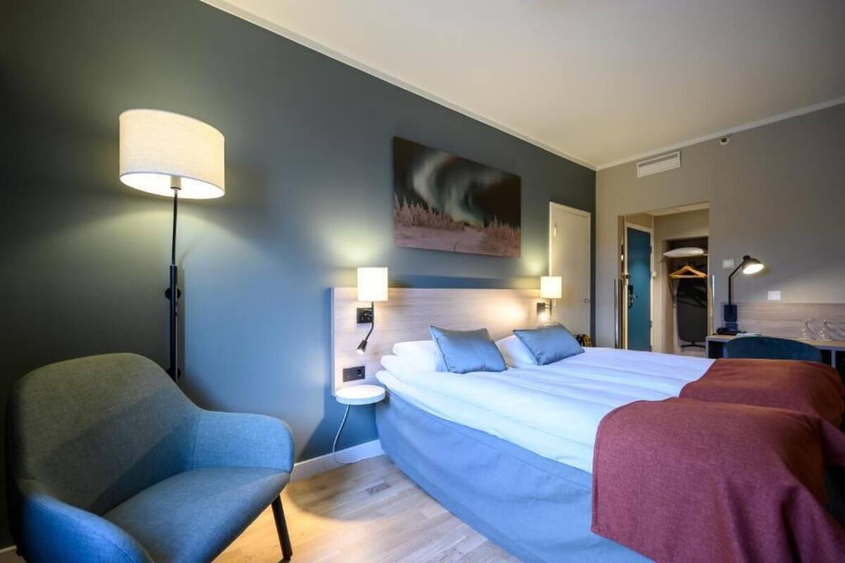 A hotel room with a large bed, a chair, bedside lamps, a painting on the wall, and a wardrobe.
