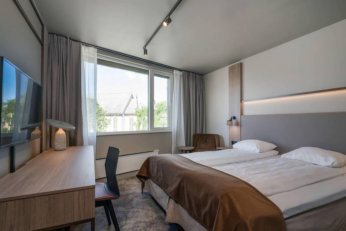 A hotel room with a bed, a desk, a chair, a TV, and a window with curtains.
