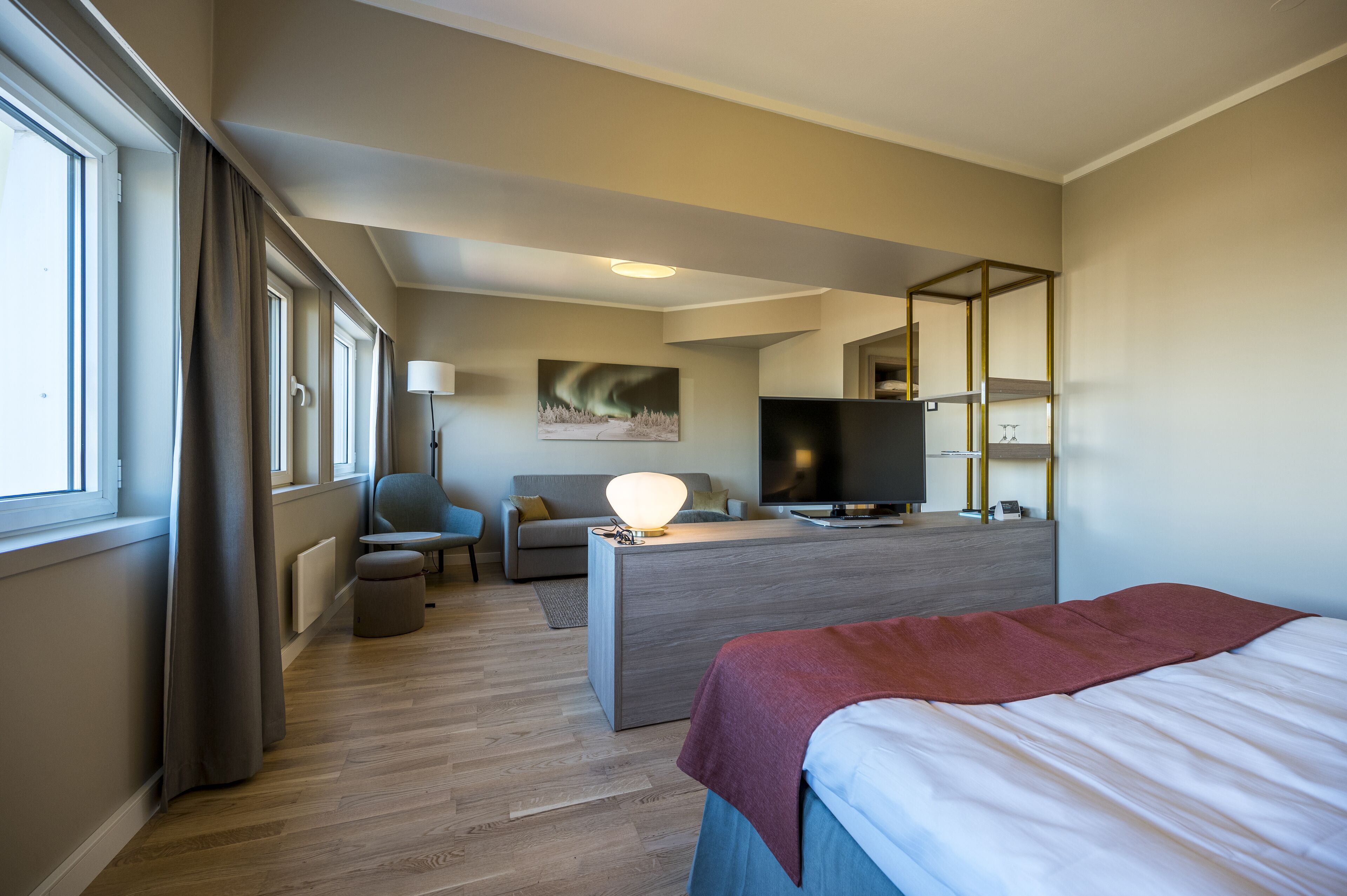 A modern hotel room with a bed, a desk, a sofa, and a TV.