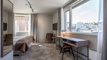 Una habitación de hotel moderna con un ventanal grande, un escritorio, una silla, una cama y un espejo.