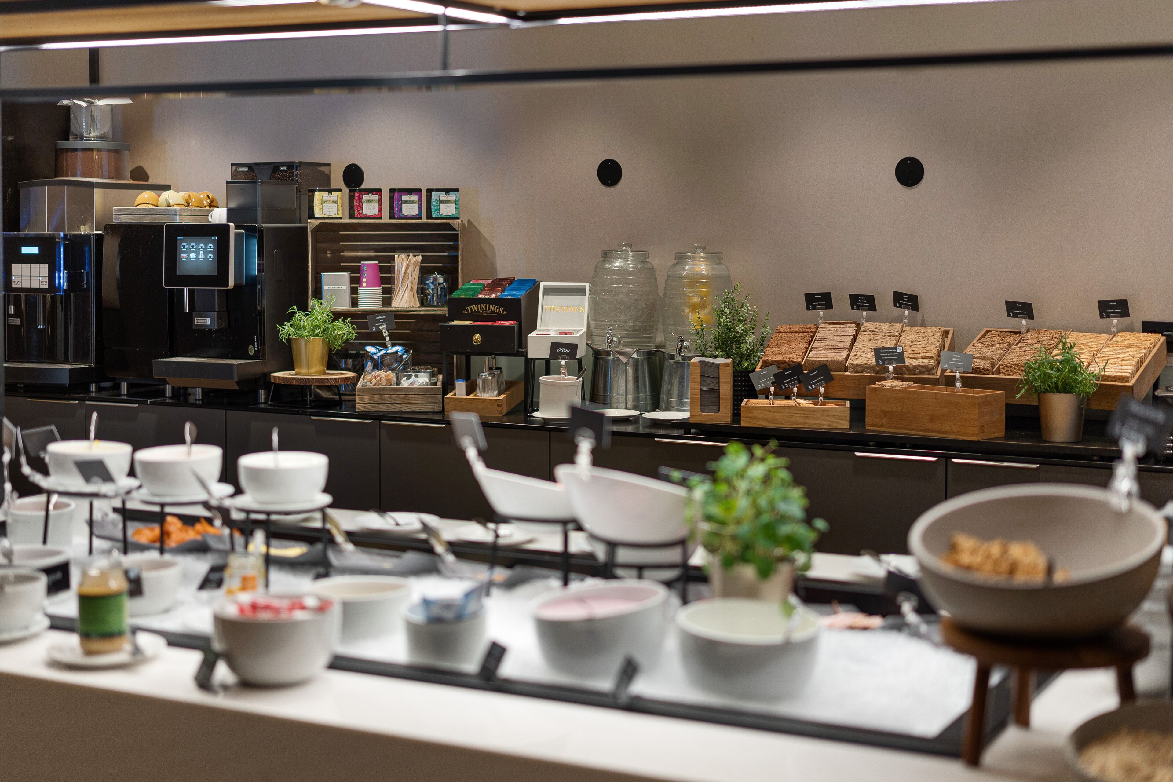 A buffet setup with various food items, a coffee machine, and a self-service beverage station.