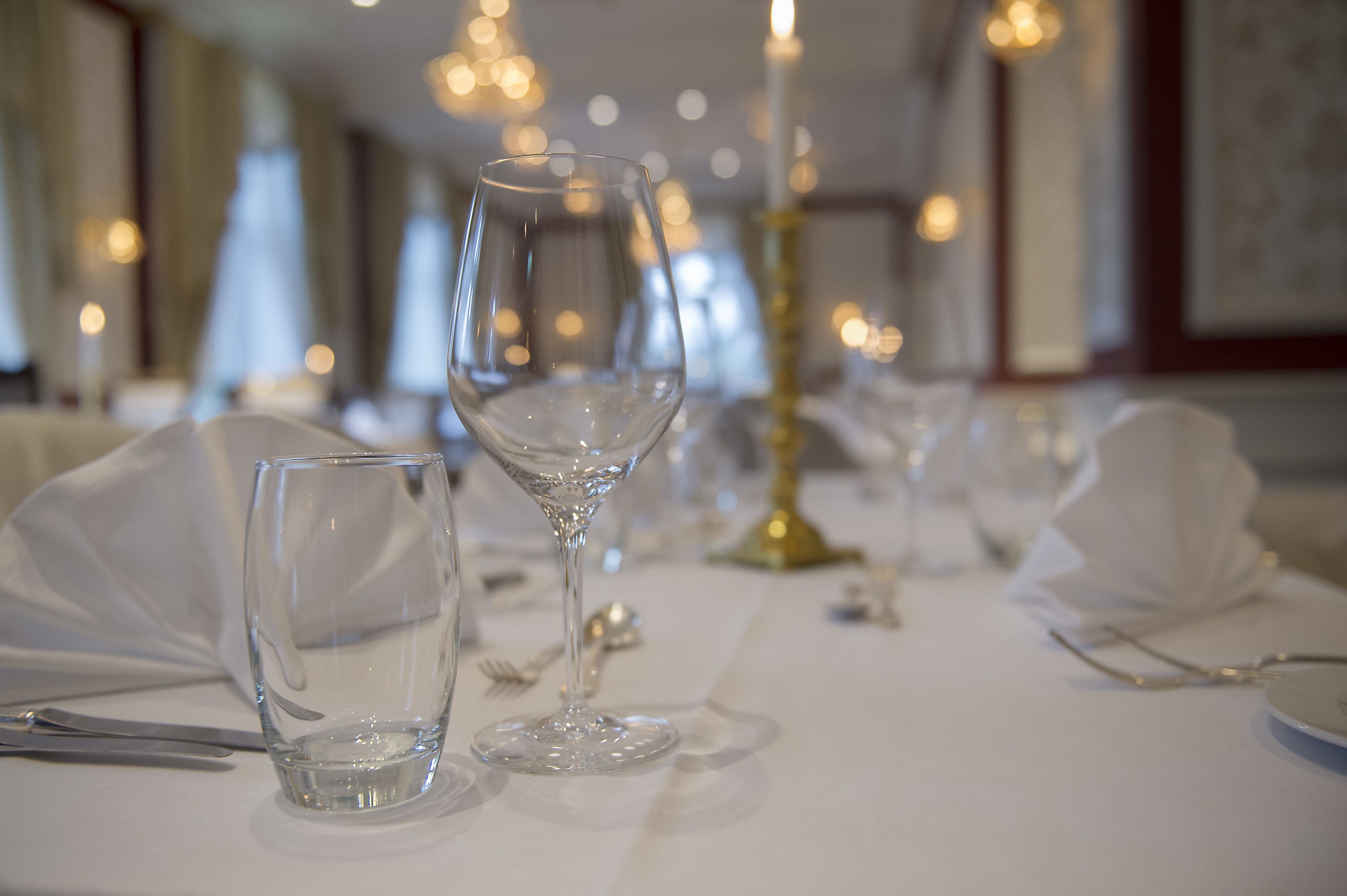 Een eettafel gedekt met helder glaswerk, een gouden kandelaar en witte tafelkleden.