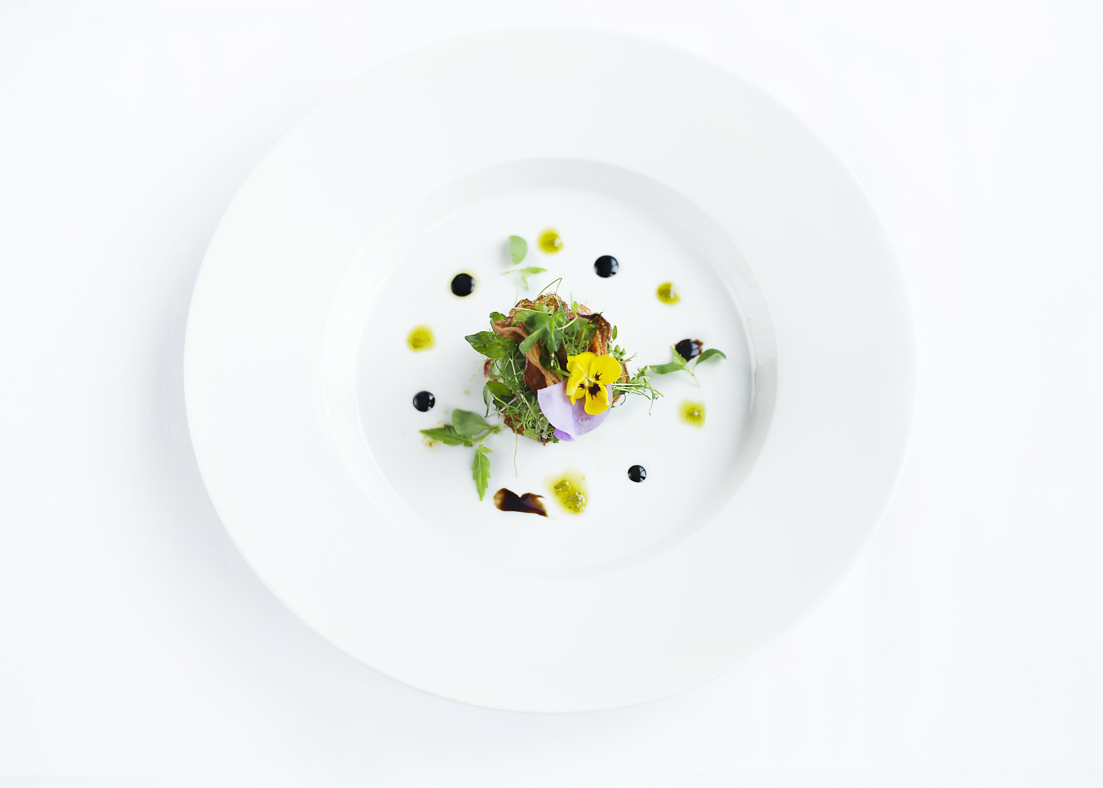 A white plate with a central food arrangement, surrounded by small black and yellow dots, possibly sauces or garnishes.