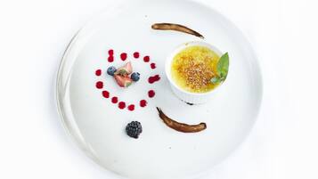 Un plato de postre con crema pastelera, frutos rojos y salsa de chocolate.