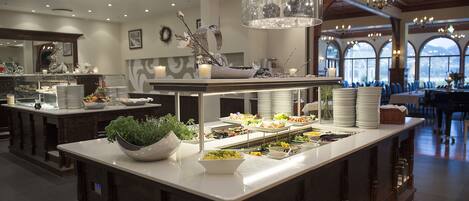 A buffet setup with various food items, a decorative centerpiece, and a chandelier.