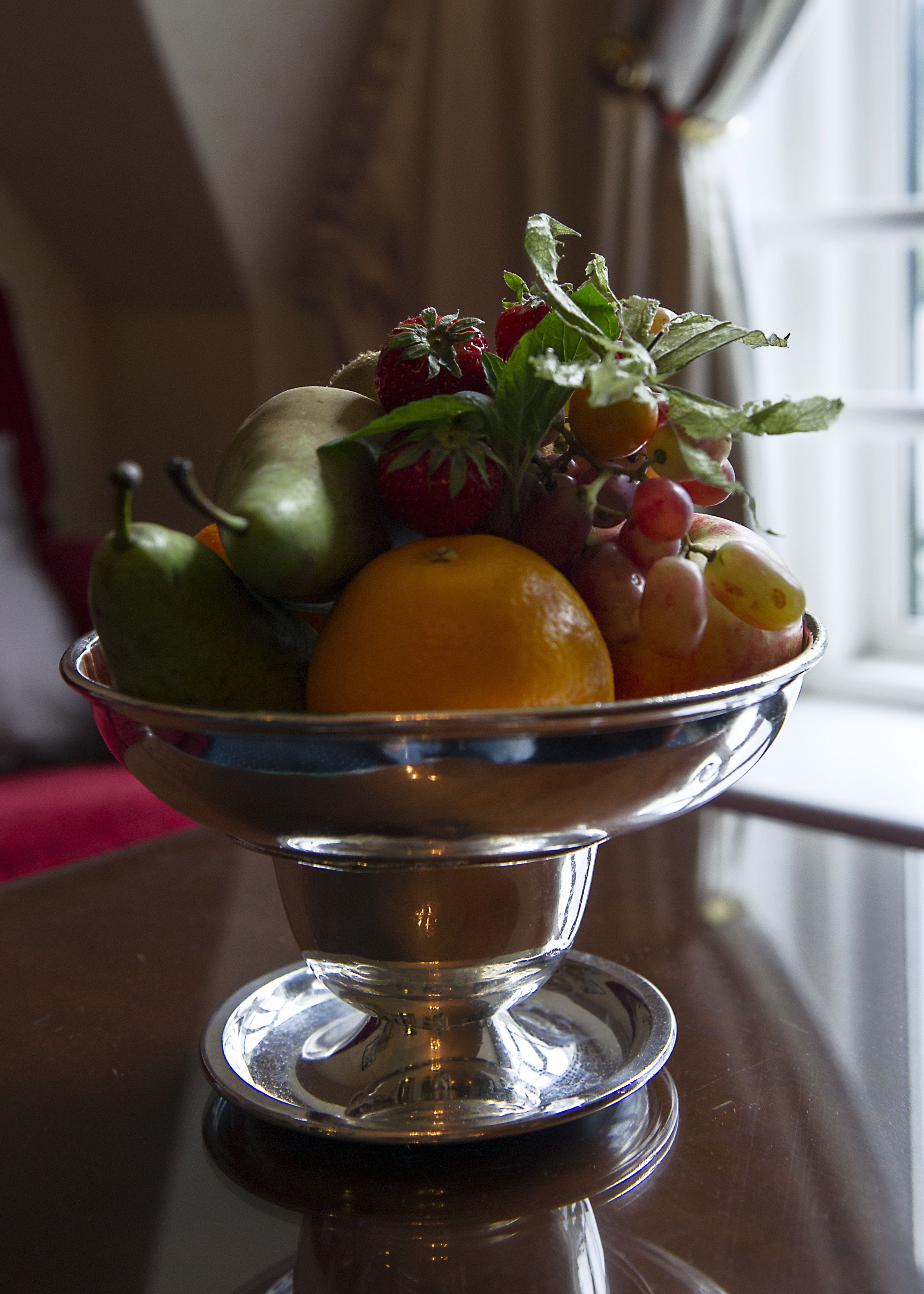 A fruit bowl on a table with a window in the background.