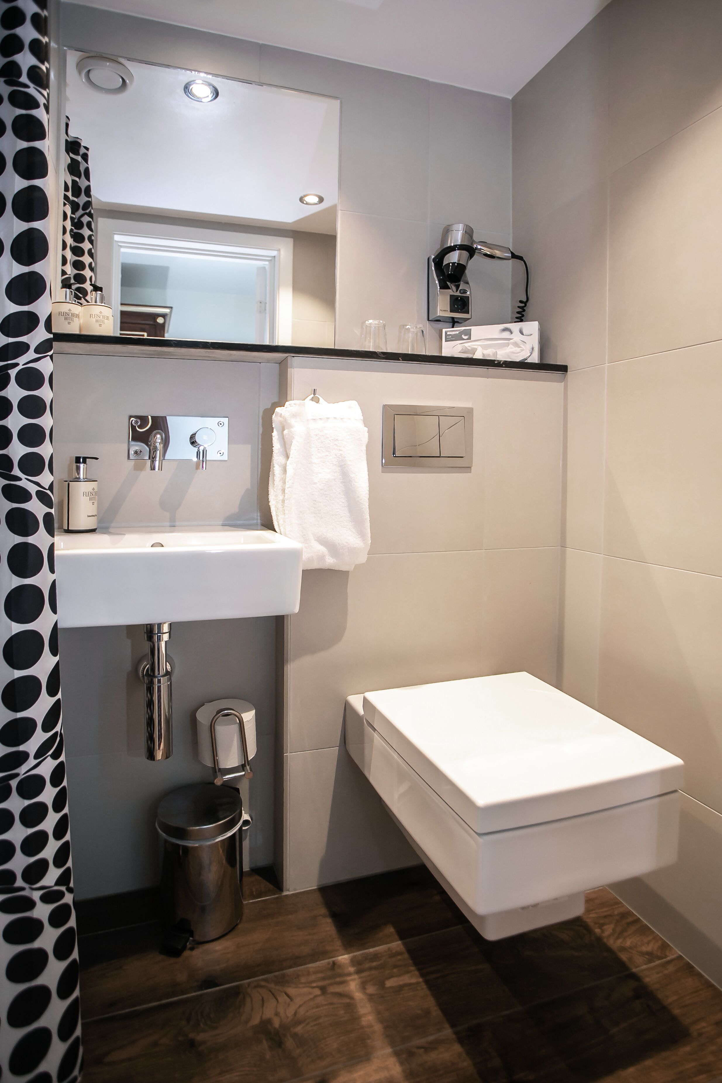 Un baño moderno con un lavabo blanco, un inodoro, una cortina de ducha, un perchero, un secador de pelo y un cubo de basura.