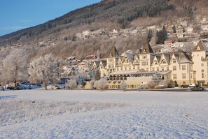 A snow-covered landscape with a row of traditional buildings featuring steep roofs and a central building with a large arched entrance. - Fleischer's Hotel (Voss)