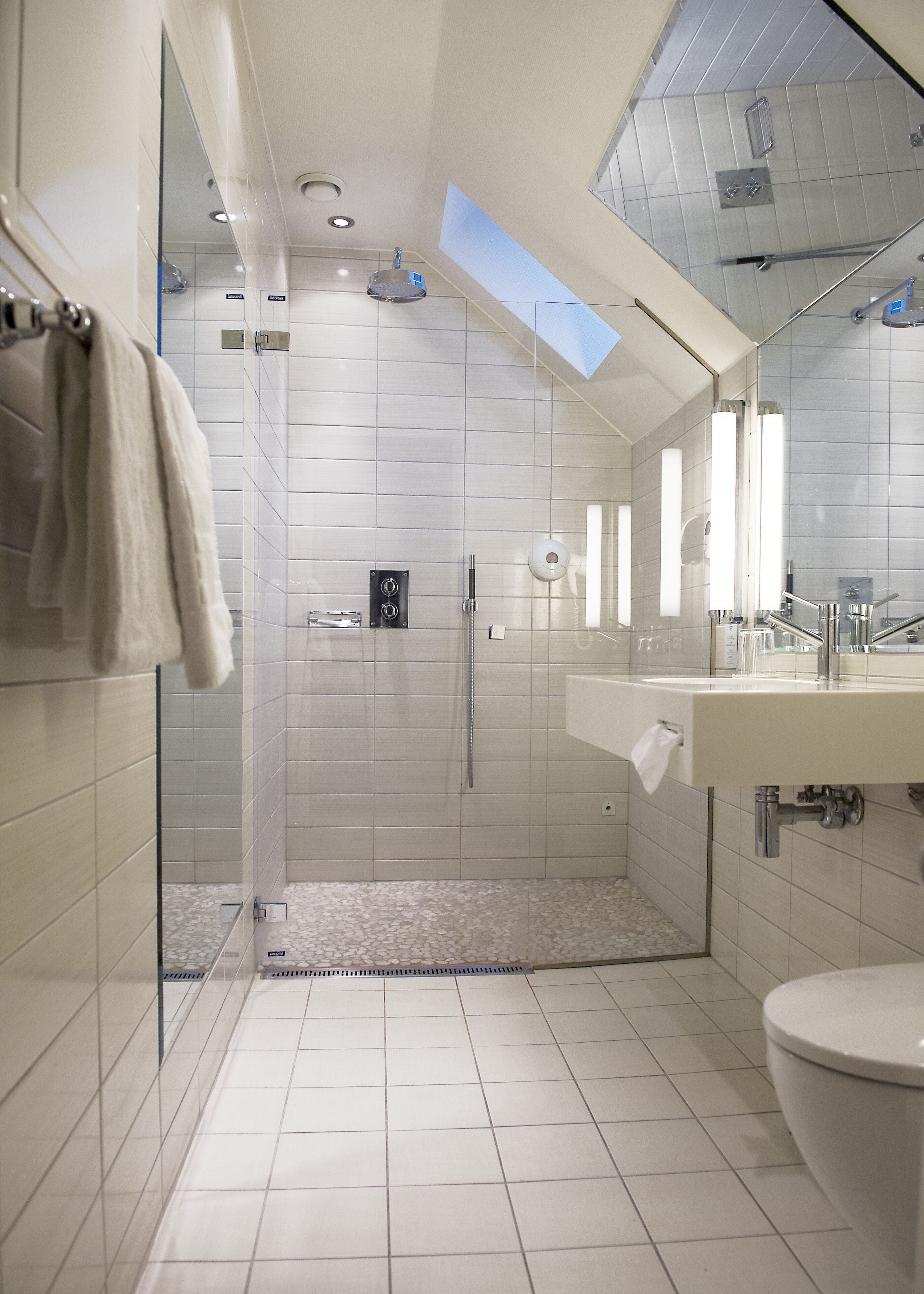 Un baño moderno con ducha de vidrio, un espejo grande y un lavamanos blanco.