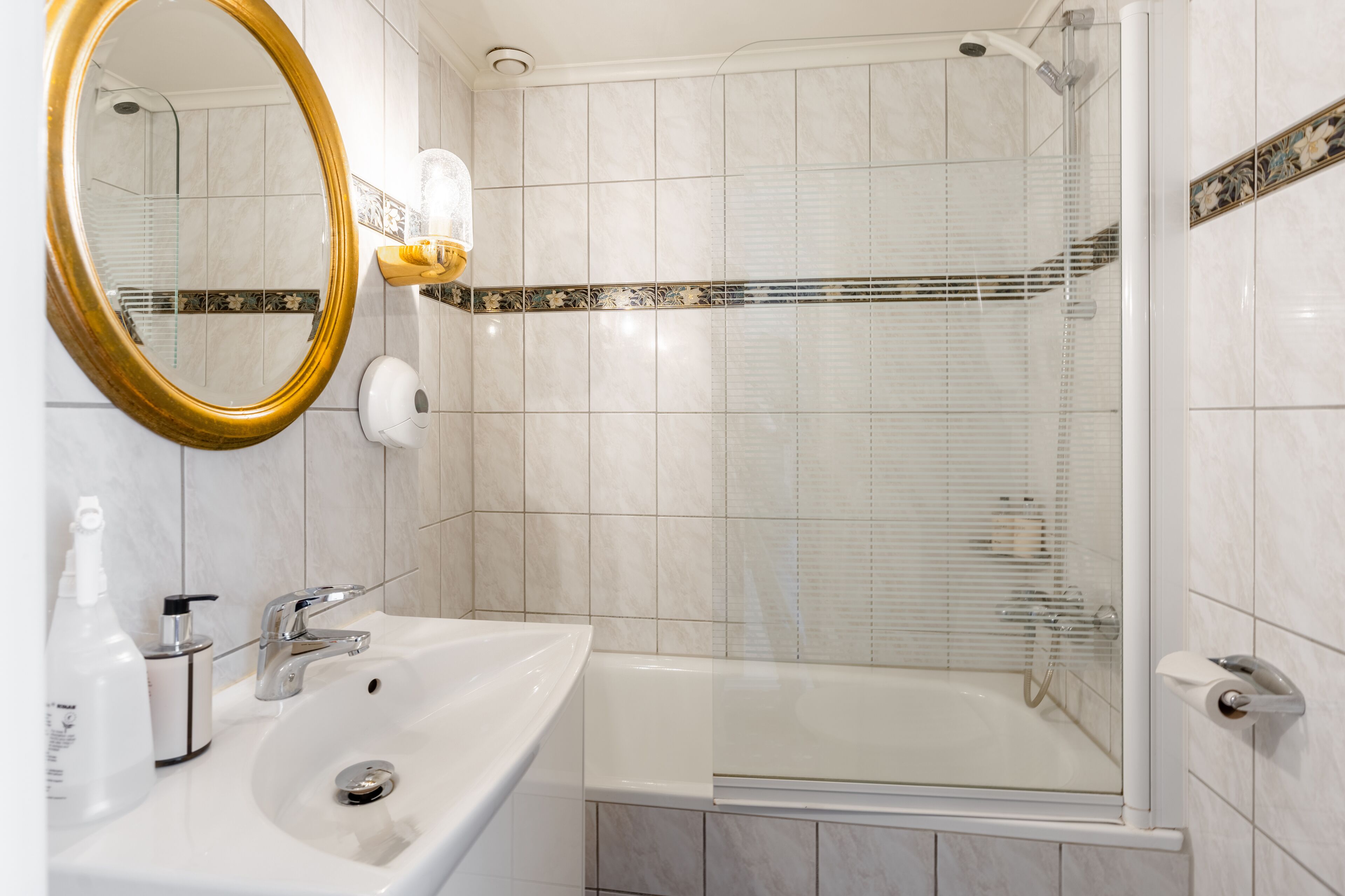 A bathroom with a white sink, a gold-framed mirror, a glass-enclosed shower, and a white bathtub.