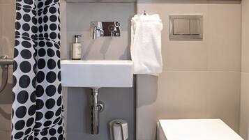A modern bathroom with a white sink, a toilet, a shower curtain with a black and white polka dot pattern, a mirror, and a hairdryer on a shelf.