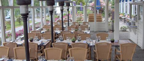 Un restaurant en plein air avec des tables et des chaises en osier, disposées sous une tonnelle bleue.