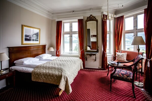 Une chambre d’hôtel avec un grand lit, une chaise, une table, un miroir et une fenêtre avec des rideaux.